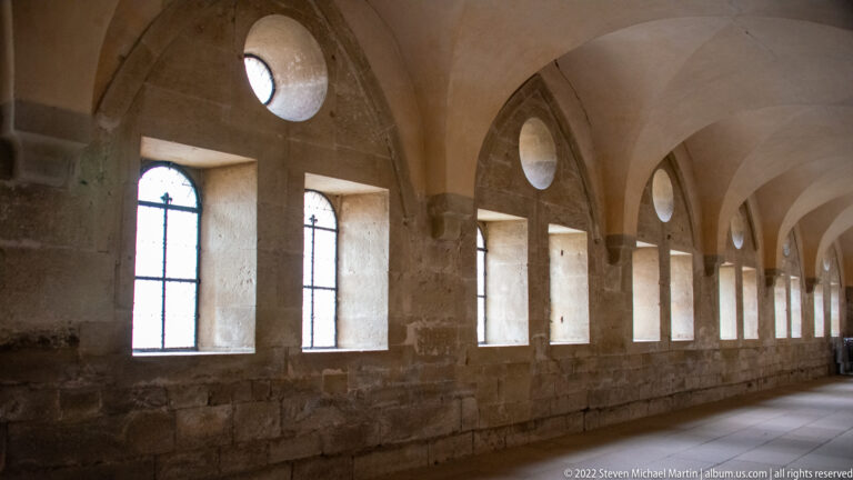 Stone hall with tall rectangular windows, pointed transverse arches, and small circular openings near the vaults.