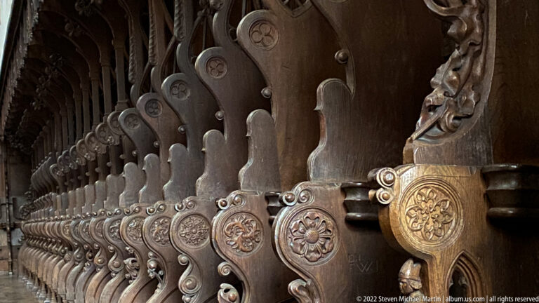 Long row of carved wooden choir stalls with repeating scroll profiles and circular floral medallions.