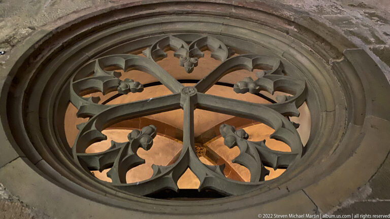 Circular Gothic stone tracery with cusped radial forms silhouetted against warm light behind.