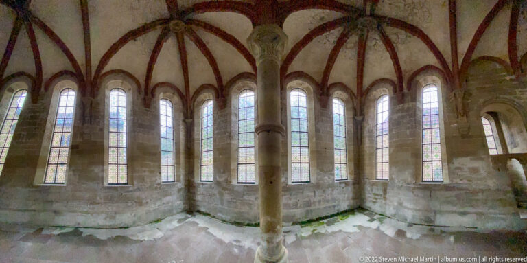 Polygonal stone interior with central column, red rib vaulting, and a continuous ring of tall narrow windows.