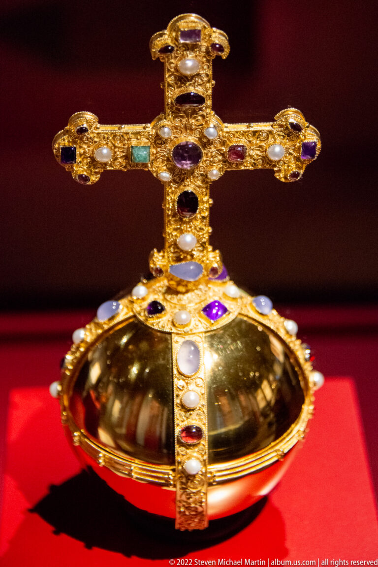 Golden jeweled orb topped by a cross, displayed on red fabric in the Imperial Castle museum.