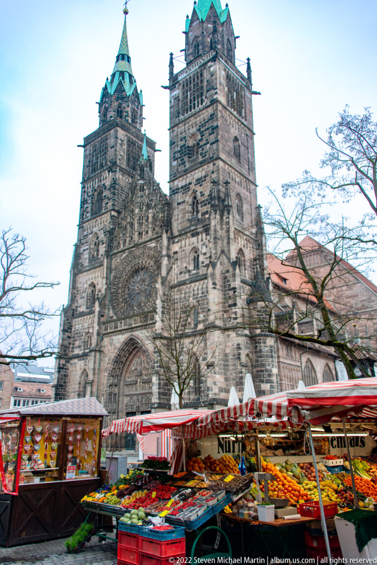 St. Lorenz twin-towered Gothic façade rising behind striped market stalls and produce stands.