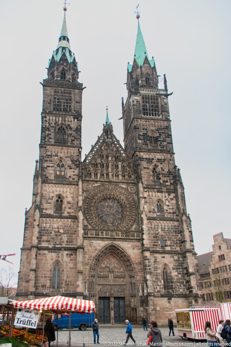 Front view of St. Lorenz with twin Gothic towers, central portal, rose window, and market canopies below.