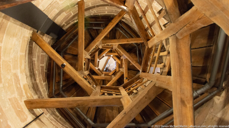 Upward view through dense heavy timber braces and stair framing inside a stone castle tower.