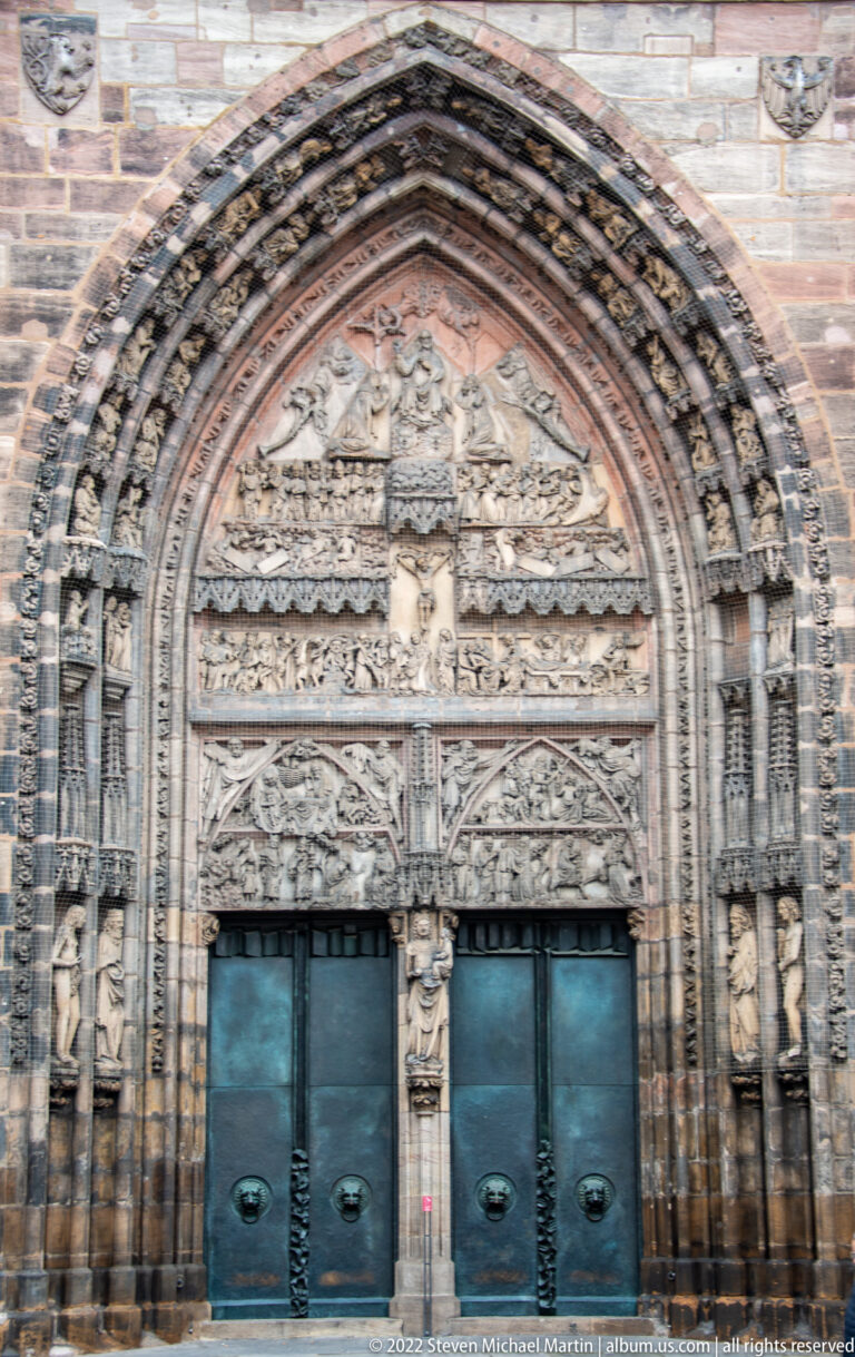 Elaborately carved pointed Gothic portal with sculpted archivolts, tympanum, jamb figures, and dark double doors.