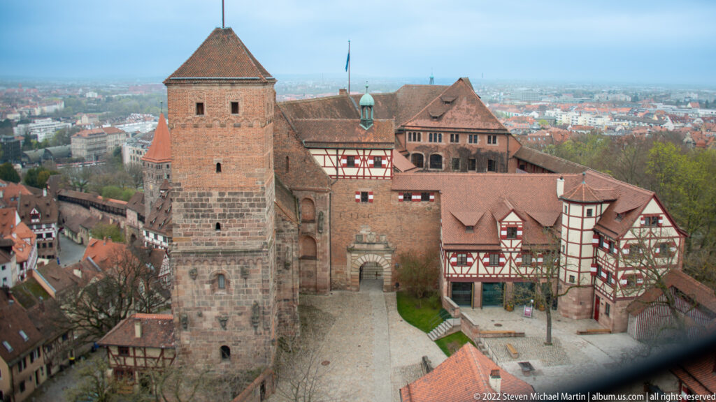 Elevated view over the Imperial Castle inner court with massive stone tower, red roofs, and half-timbered buildings.