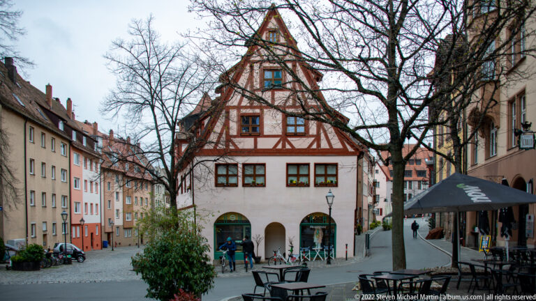Steep-gabled half-timbered house with dark framing, pale plaster, and arched openings at street level.