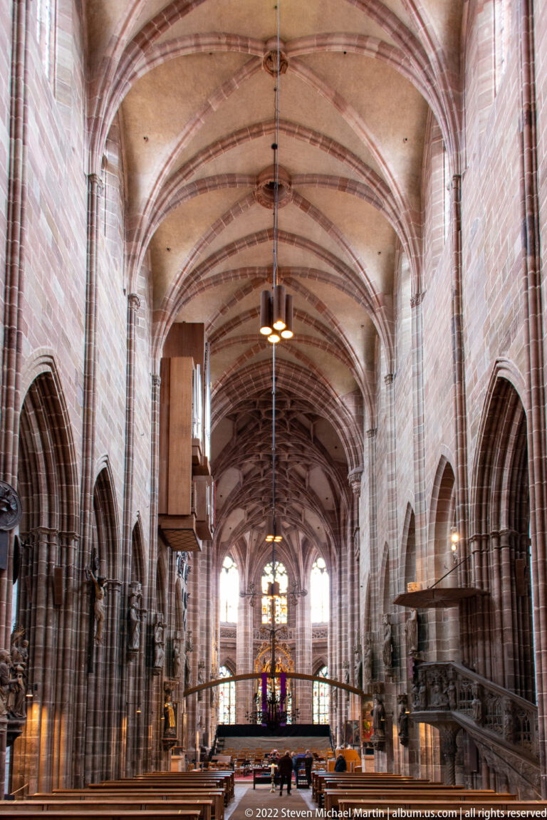 Long Gothic nave with ribbed vaults, pointed arcades, wooden pews, and stained glass in the distant choir.
