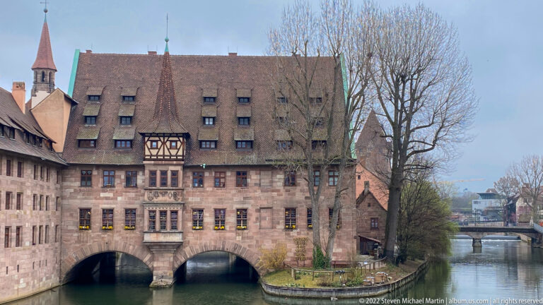 Heilig-Geist-Spital spanning the Pegnitz on twin arches with a half-timbered central bay and steep roof.