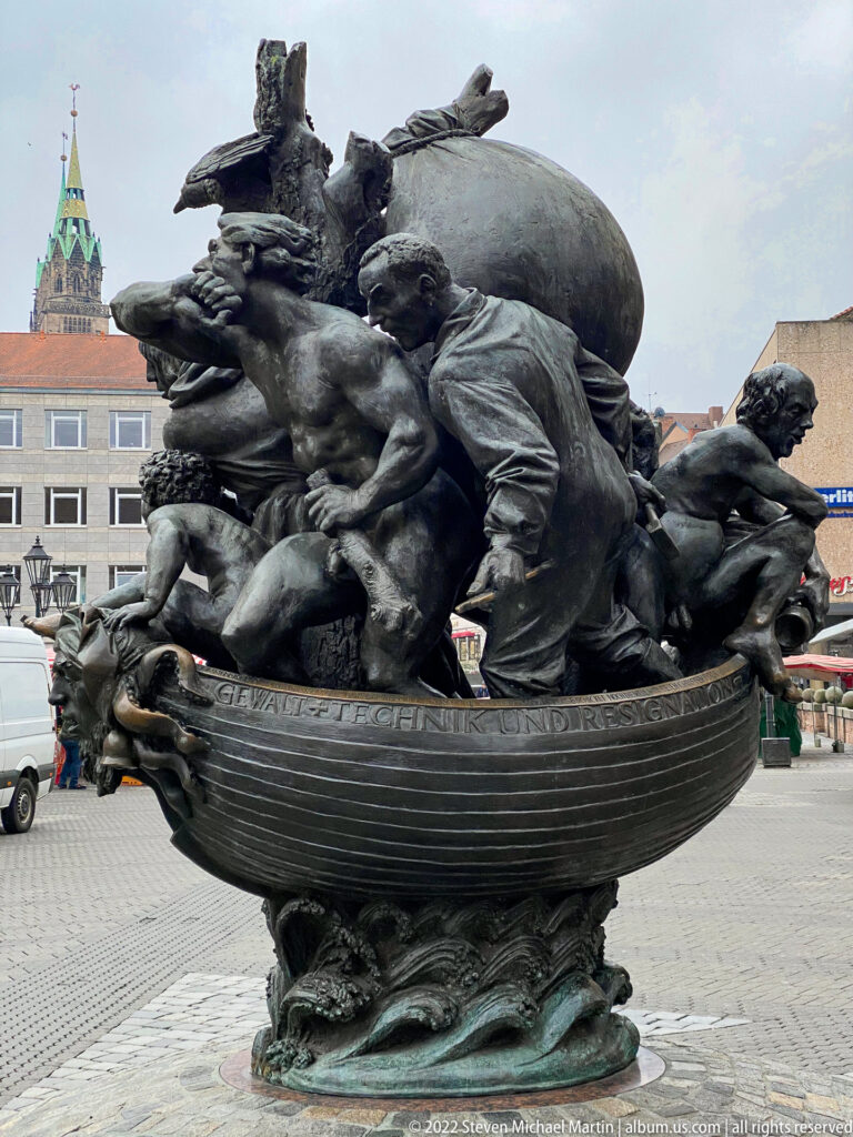 Bronze Ehekarussell fountain with intertwined human and animal figures arranged around a boat-like basin.