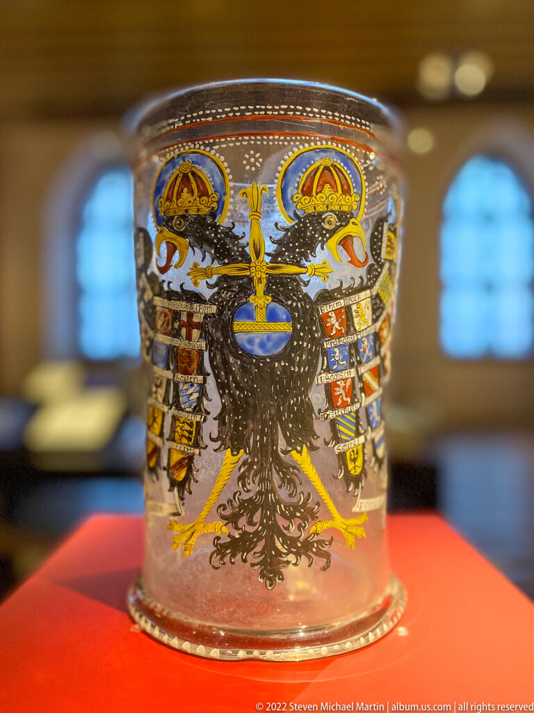 Clear cylindrical beaker painted with a black double-headed imperial eagle, colorful shields, and gold ornament.