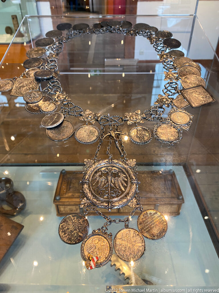Elaborate metal ceremonial chain with many portrait medallions, heraldic discs, and a large central pendant.