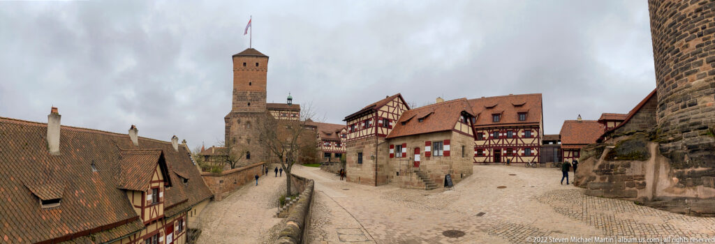 Imperial Castle courtyard with cobblestone paths, red-roofed historic buildings, and the Sinwell Tower rising behind.