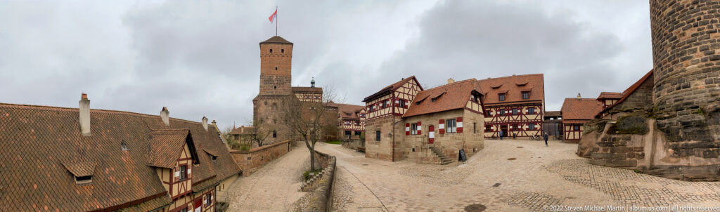 Wide view of the Imperial Castle precinct with Sinwell Tower, steep roofs, stone walls, and half-timbered buildings.