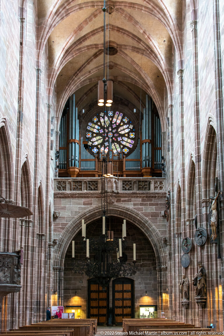West interior of St. Lorenz with organ pipes, large rose window, entry doors, and ribbed nave vaults.