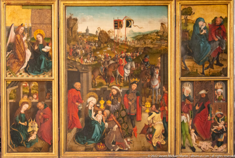 Painted winged altarpiece with central Nativity and Adoration scene and smaller narrative panels at both sides.
