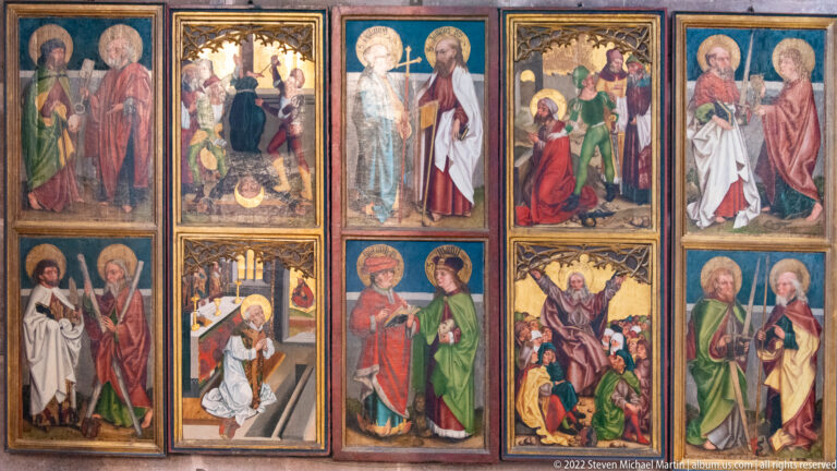 Ten narrow painted panels showing haloed saints, bishops, and sacred narrative scenes in gold-framed compartments.