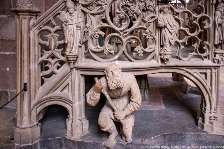Kneeling carved support figure beneath dense late-Gothic tracery at the base of a stone sacrament house.