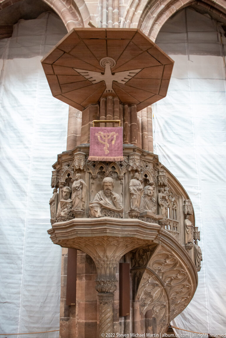 Carved stone pulpit with relief figures, curving stair, and broad wooden sounding board inside St. Lorenz.