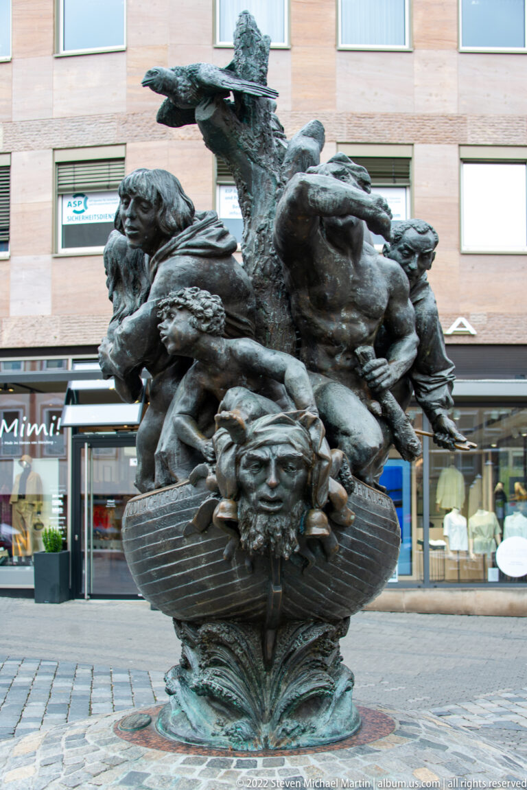 Bronze Ehekarussell fountain with intertwined figures, animals, and expressive faces on a circular base.