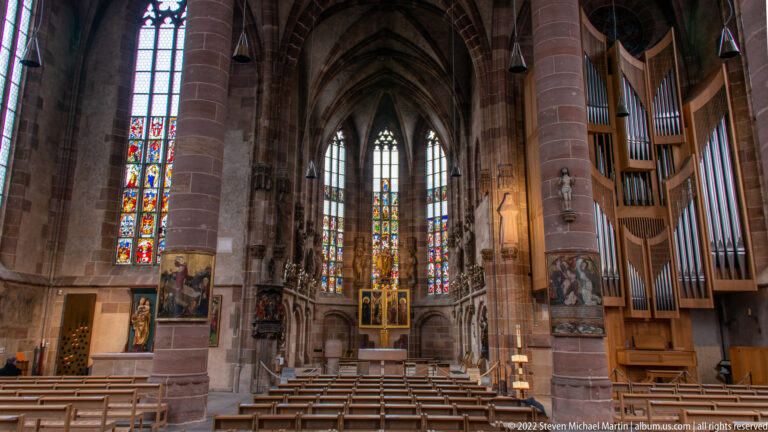 St. Sebald interior with pointed vaults, wooden seating, stained glass, and a large pipe organ at right.