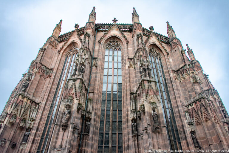 Upward view of St. Sebald’s high Gothic choir with tall traceried windows, buttresses, pinnacles, and sandstone masonry.