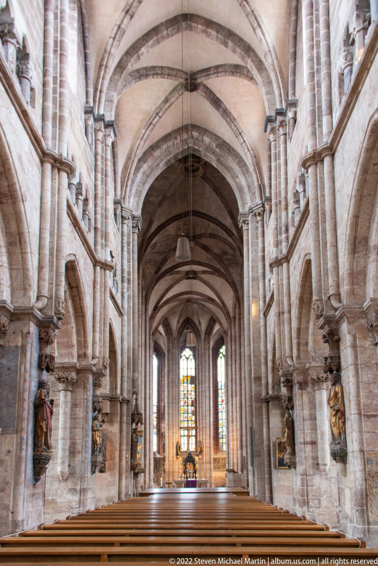 Central nave of St. Sebald with broad arches, ribbed vaults, sandstone piers, pews, and stained glass at the far end.