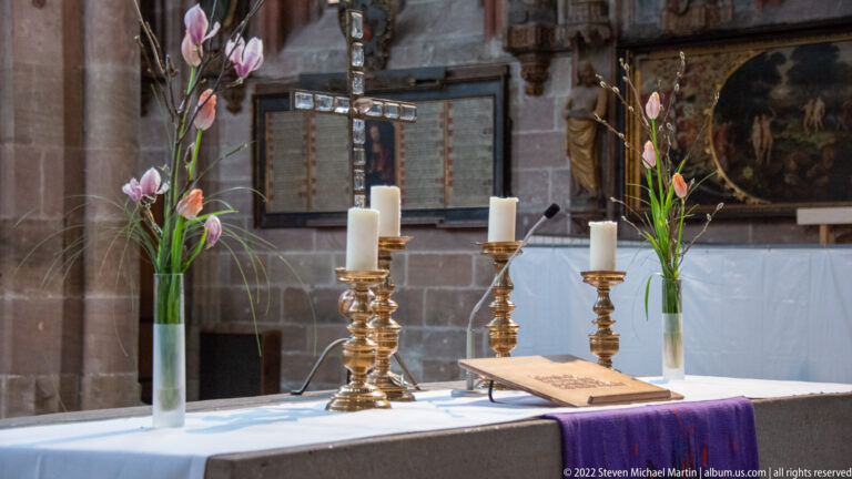 Altar table with brass candlesticks, white candles, tulips, open book, and purple frontal inside St. Sebald.
