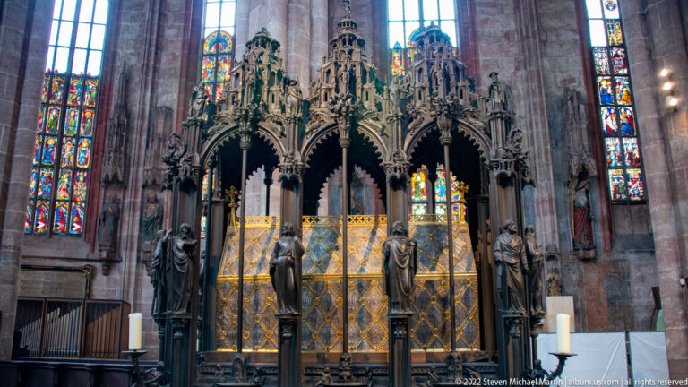 Front view of Saint Sebald’s bronze tomb with tall openwork canopy, standing figures, gilded shrine, and stained glass.