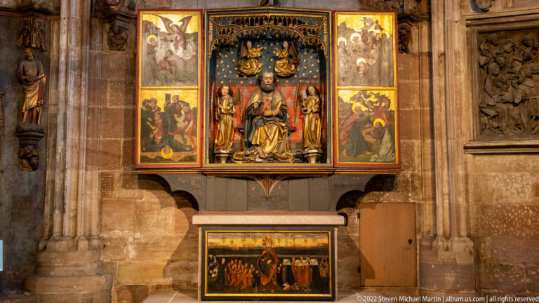 Painted and carved winged altarpiece with central seated figure, standing saints, side-panel paintings, and predella.