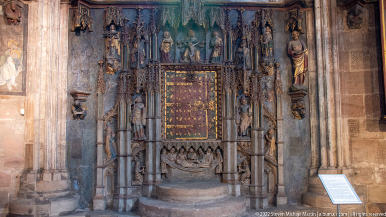 Elaborate Gothic stone wall monument with central panel, flanking saints, pinnacles, and a painted upper section.