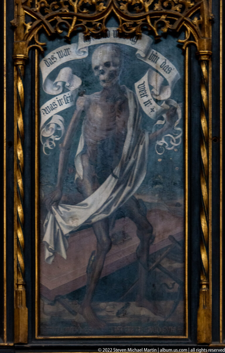 Dark framed devotional painting with central robed figure, clouds, and ribbon-like German inscriptions.