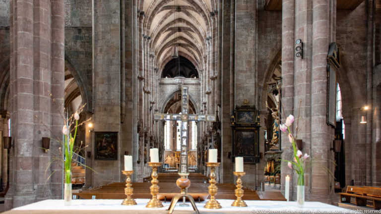 White altar with brass candlesticks and flowers aligned with the long Gothic nave and choir of St. Sebald.