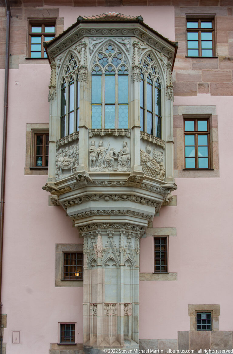 Ornate projecting stone Chörlein with Gothic tracery, pinnacles, sculpted bracket, and polygonal windows.