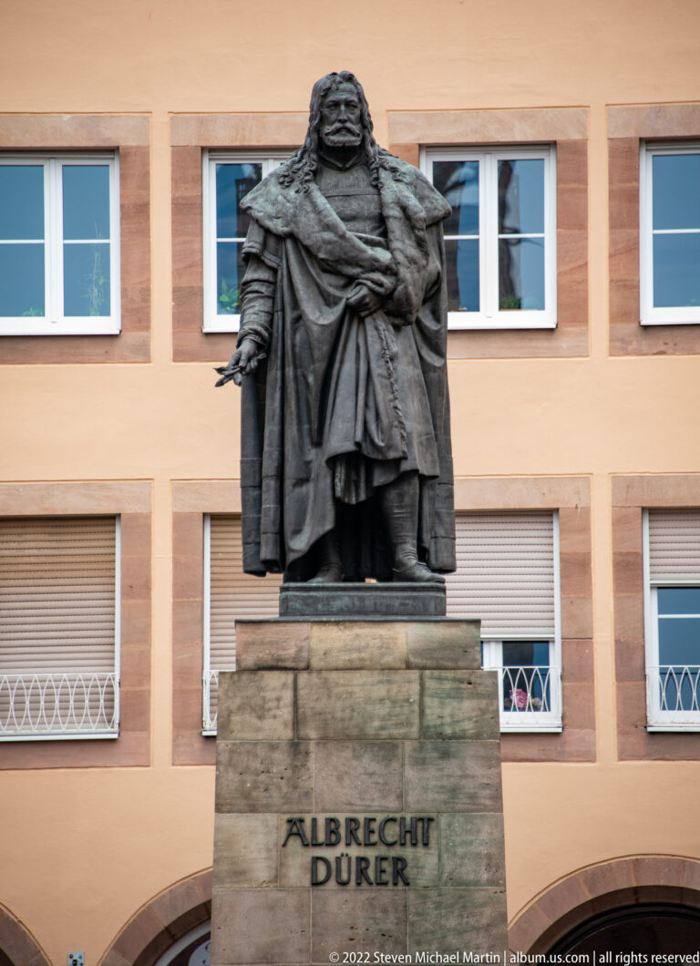 Bronze statue of Albrecht Dürer in a cloak on a stone pedestal inscribed ALBRECHT DÜRER.