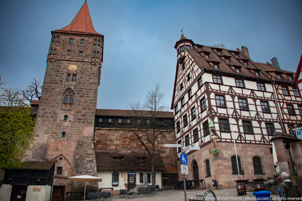 Square medieval stone tower beside half-timbered houses in Nuremberg’s Tiergärtnertor castle district.