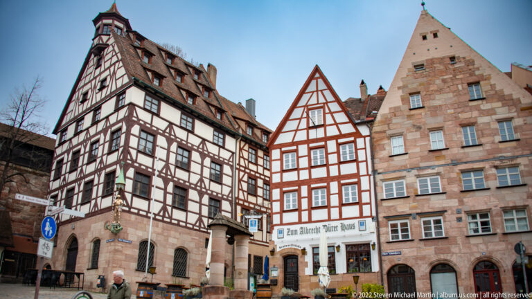 Three adjoining historic houses with contrasting half-timbered and stone façades beneath steep gabled roofs.