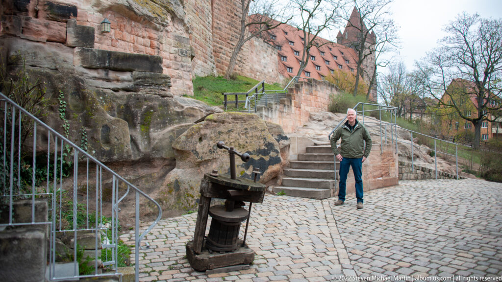 Cobblestone path, stone steps, heavy castle walls, and a weathered historic mechanism in the Imperial Castle precinct.