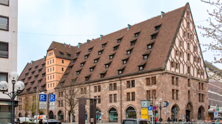 Long Mauthalle building with steep tiled roof, rows of dormers, tall gable, and arched ground floor.