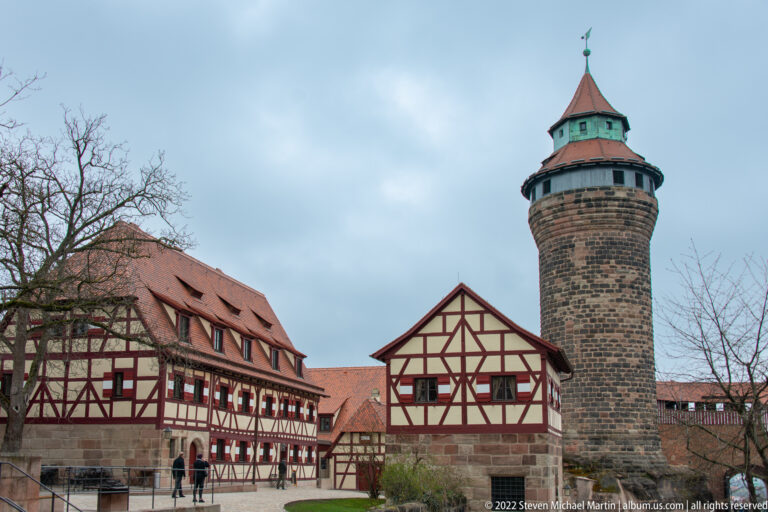 Round Sinwell Tower with polygonal upper stage and red roof rising above half-timbered castle buildings.