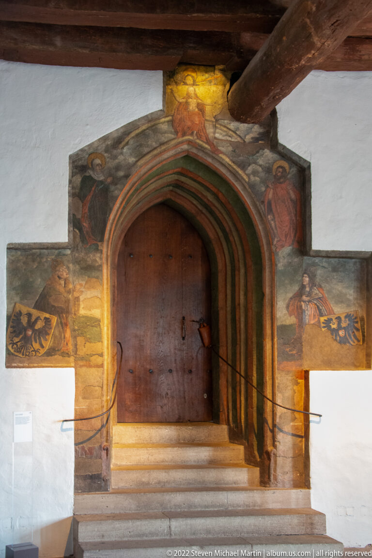 Pointed wooden doorway framed by painted stone bands, standing figures, and heraldic eagles inside the Imperial Castle.