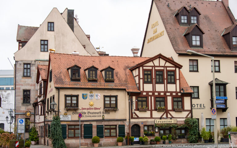 Cluster of historic Regensburg buildings with tiled roofs, half-timbering, painted signs, and street-level restaurant and hotel entrances.