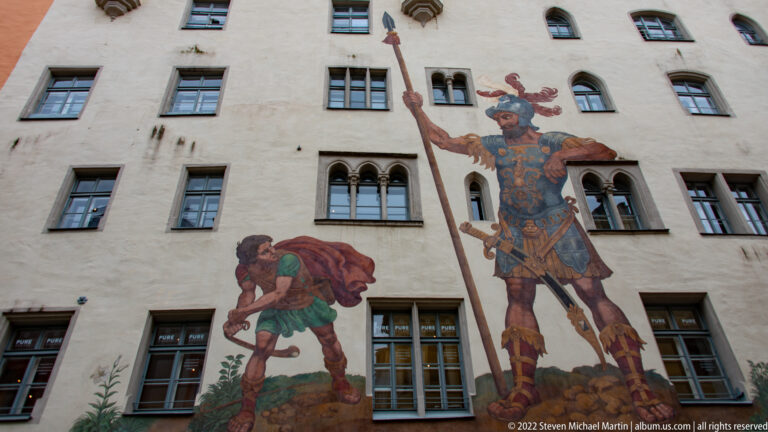 Large painted David and Goliath scene covering the façade of the Goliathhaus, with the armored giant towering over David.