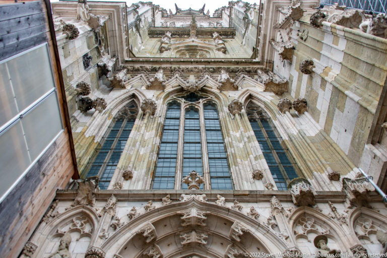 Steep upward view of Regensburg Cathedral showing tall traceried windows, carved stone figures, pinnacles, and pointed arches.