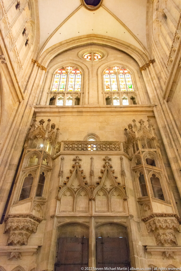 Tall carved stone wall monument with pointed arches, tracery, small figures, recessed panels, and windows above.