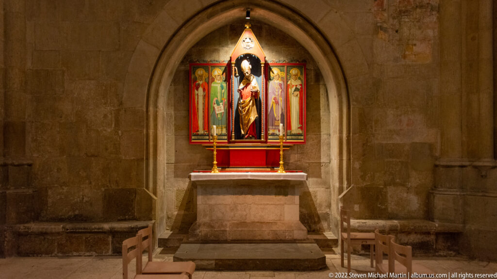 Small cathedral side chapel with a bright painted-and-sculpted altarpiece set in a pointed stone recess above a simple altar.