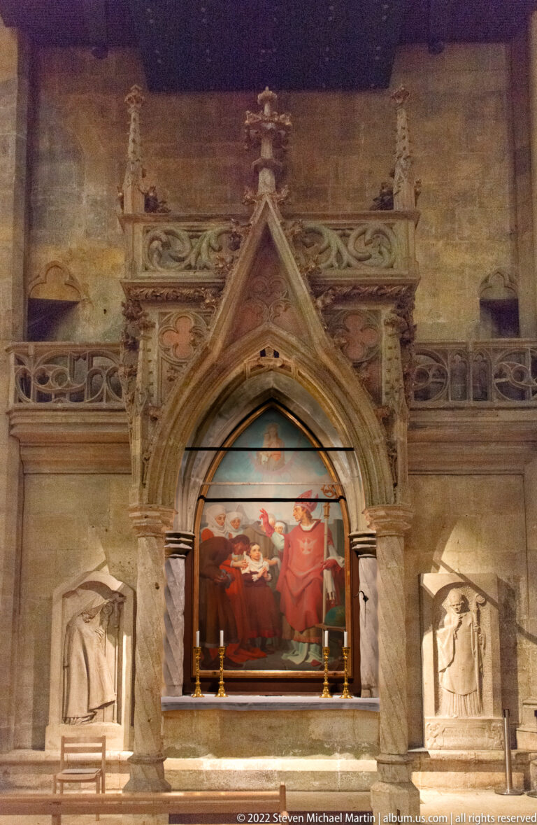 Side altar with a central religious painting, pointed Gothic stone frame, and sculpted figures in recessed niches on both sides.