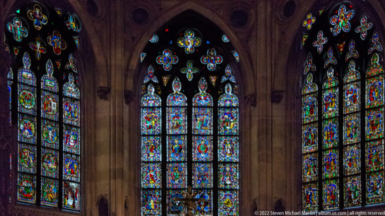 Three tall stained-glass window groups with pointed arches, stone mullions, and vivid figurative panels.