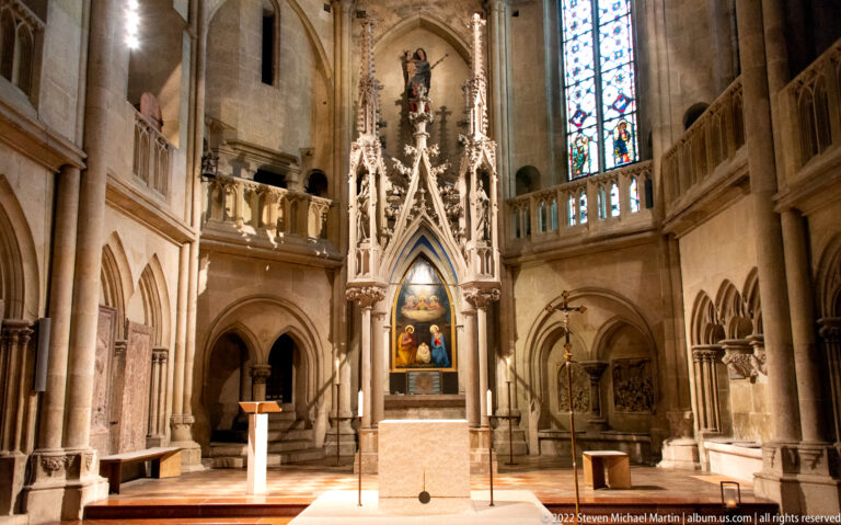 Ornate Gothic side altar with painted devotional panel, pinnacles, pointed arches, balustrades, and stained glass.