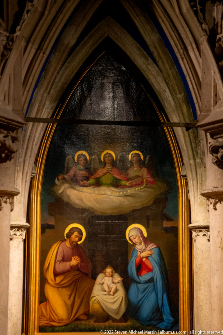 Pointed-arch religious painting with Mary, Joseph, infant Jesus, and three angels above.